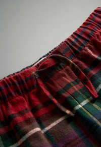 Pantalones cortos de pijama a cuadros rojos y verdes con una cintura elástica, que presentan un detalle de lazo y una tela suave y texturizada.