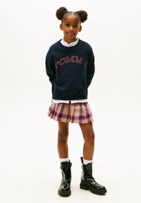 Felpa navy con logo "TOMMY", gonna a pieghe rosa a quadri, stivali neri alla caviglia e calzini bianchi. Design semplice, vestibilità informale e look a strati.
