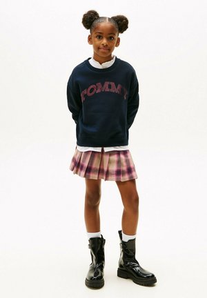 Felpa navy con logo "TOMMY", gonna a pieghe rosa a quadri, stivali neri alla caviglia e calzini bianchi. Design semplice, vestibilità informale e look a strati.