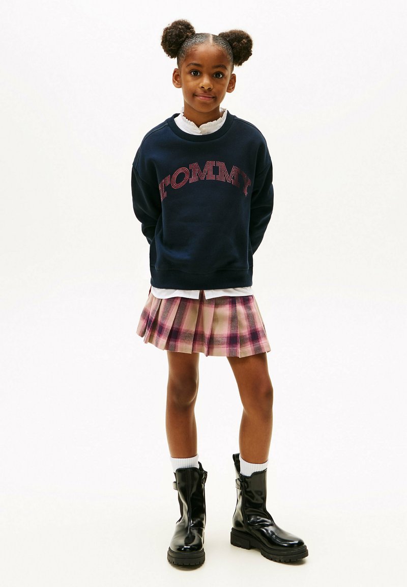Felpa navy con logo "TOMMY", gonna a pieghe rosa a quadri, stivali neri alla caviglia e calzini bianchi. Design semplice, vestibilità informale e look a strati.