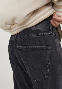 Černé džíny z denimu se sepraným vzhledem, se zadními kapsami, koženou nášivkou v pase a texturovaným svetrem s proužkovanými manžetami.