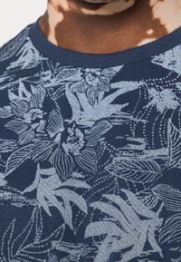 Navy blue t-shirt featuring a floral design in light blue, with detailed leaves and flowers, crew neckline, made from textured fabric.