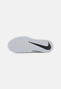 Weiße Sport-Schuhsohle mit einem wellenförmigen Muster, ausgestattet mit einem schwarzen Nike-Swoosh-Logo. Texturierte Oberfläche für besseren Halt und Traktion.