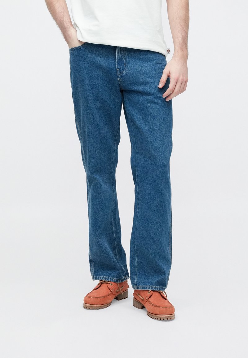 Blue denim jeans with a straight-leg cut, featuring a classic five-pocket design and a slightly faded finish. Paired with orange loafers.