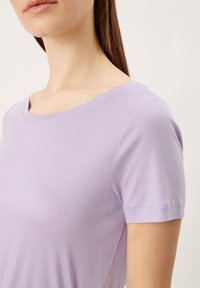 Majica s kratkim rukavima lavande boje s širokim izrezom, izrađena od glatkog materijala s blagim rastezljivim svojstvom, s uredno šivenim rubovima.