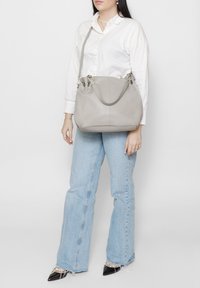Sac à main en cuir gris avec un design décontracté, texture lisse, double poignée et détails en métal argenté. Comprend une bandoulière ajustable.