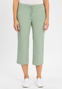 Lichtgroene cropped broek met een elastische tailleband en een trekkoord. Soepele stof, rechte snit en opgerolde zoom; gedragen met witte sneakers.