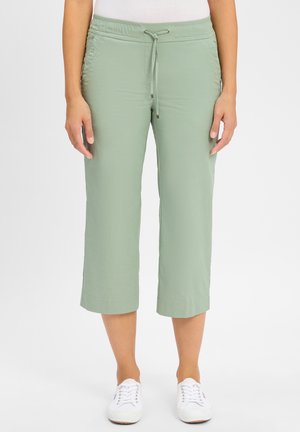 Lichtgroene cropped broek met een elastische tailleband en een trekkoord. Soepele stof, rechte snit en opgerolde zoom; gedragen met witte sneakers.