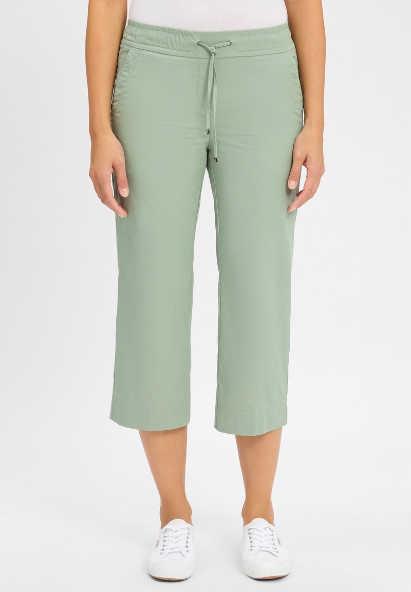 Lichtgroene cropped broek met een elastische tailleband en een trekkoord. Soepele stof, rechte snit en opgerolde zoom; gedragen met witte sneakers.