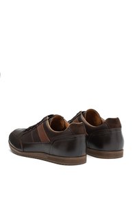 Scarpe casual in pelle marrone scuro con design allacciato e dettagli in suede marrone, fotografate da dietro su uno sfondo bianco.