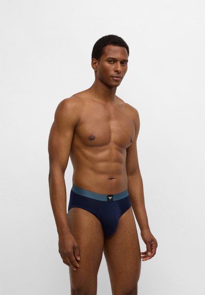 Tamsiai mėlynos trumpikės su turkio spalvos juosmeniu ir subtiliu prekės ženklo akcentu; pagamintos iš lygaus audinio su elastingu tamprumu patogumui.