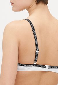 Reggiseno bianco con spalline nere regolabili, caratterizzato dal logo "Copenhagen Studios". Include una chiusura semplice con gancio sul retro.
