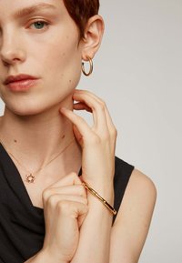 Pendientes de aro de oro, un collar con un colgante en forma de estrella con acentos de colores, y una pulsera de brazalete de oro, en una modelo que lleva una blusa negra.