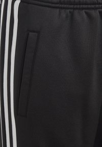 Pantalones de chándal negros de tela texturizada, con un bolsillo lateral y rayas blancas verticales a lo largo de las costuras exteriores para contraste.