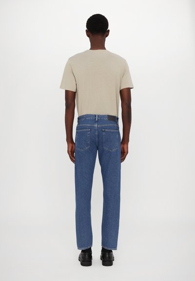 Camiseta de manga corta color beige claro combinada con jeans de mezclilla azules de corte recto. Los jeans tienen una cinturilla oscura y dos bolsillos traseros.