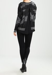 Černý a šedý maskáčový svetr s volnějším střihem, kulatým výstřihem a detailem otevřených zad. Kombinováno s černými úzkými džínami a kotníkovými botami.