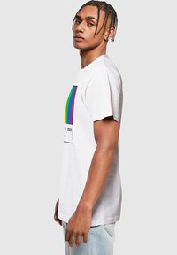 Witte katoenen t-shirt met een rechthoekige grafiek met regenboogstrepen en de tekst "PRIDE 2024". Korte mouwen, ontspannen pasvorm, minimalistisch ontwerp.