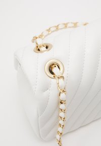 Biała pikowana skórzana torebka z złotym łańcuchem i okrągłymi oczkami. Teksturowana powierzchnia z ukośnymi szwami.