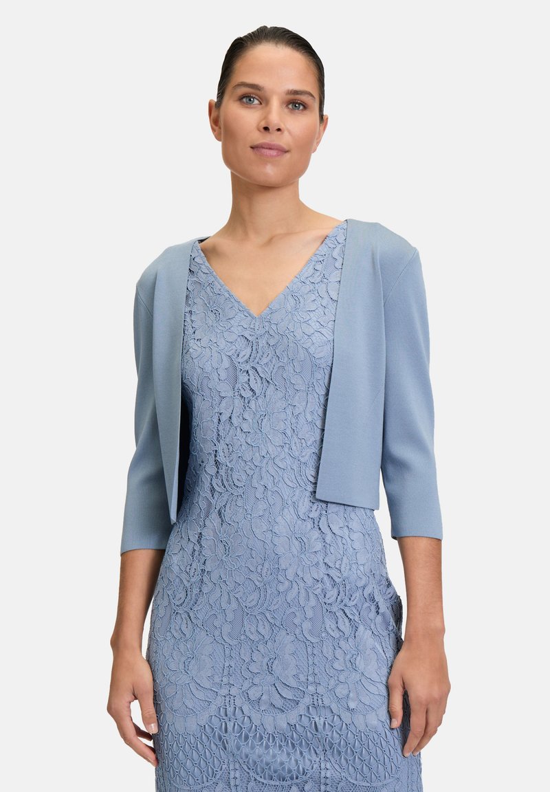 Lys blå kort cardigan med trekvartærmer, lagd over en matchende blonderkjole med blomster mønstre og V-halsudskæring.