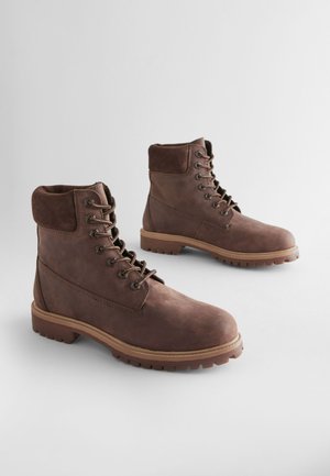 Bottes basses en cuir marron avec une finition texturée, col matelassé, œillets métalliques et semelle en caoutchouc robuste. Design élégant pour une durabilité optimale.