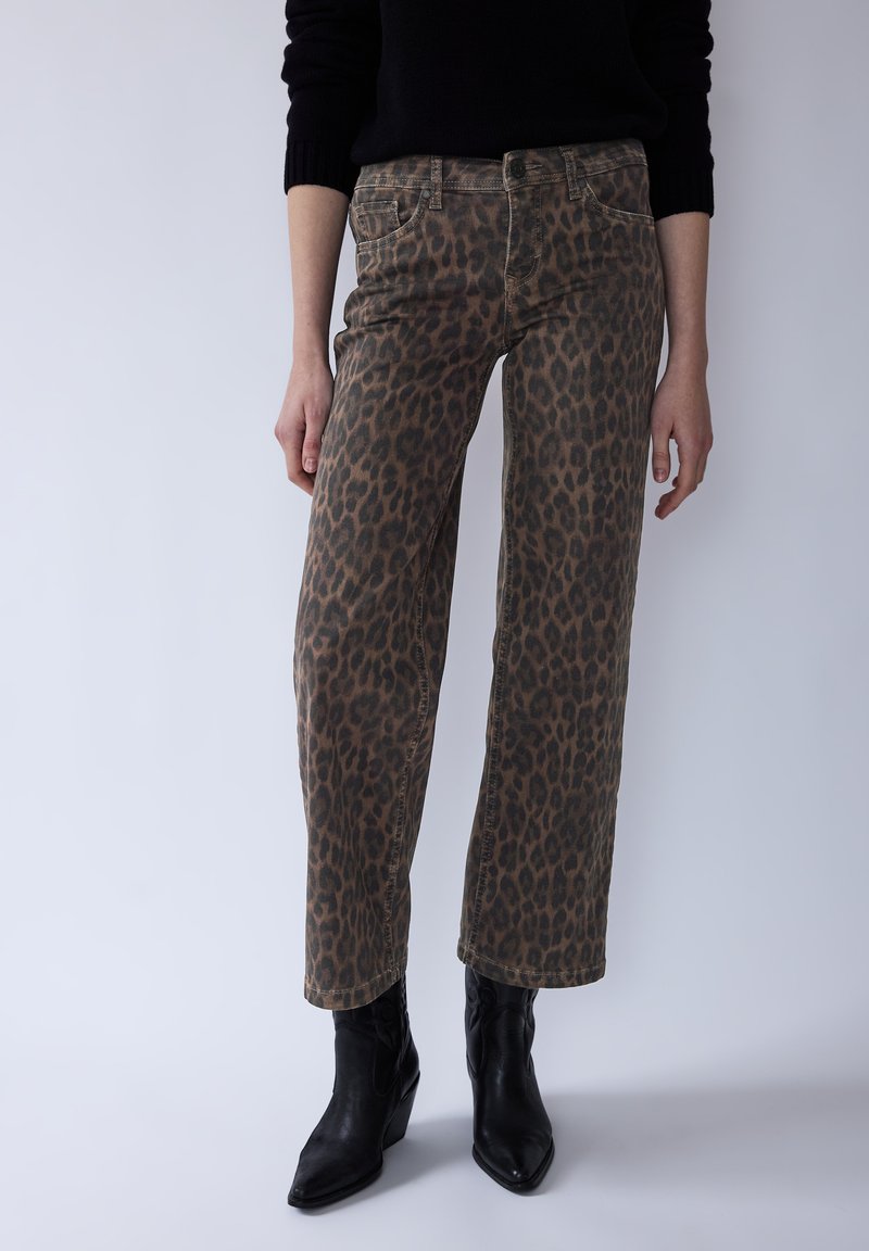 Džíny s leopardím vzorem s širokými nohavicemi v hnědé a černé barvě, vyrobené z bavlněné směsi. Mají přední kapsy a zapínání na knoflíky. Kombinovány s černými kotníkovými botami.