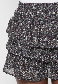 Minifalda negra con flores y volantes en capas. Presenta una tela ligera y transparente con patrones florales multicolores y una cinturilla elástica.