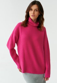 Oversized pink sweater with a cowl neck, made from soft knit fabric. Features dropped shoulders and ribbed cuffs and hem.
