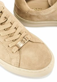 Beżowe zamszowe sneakersy z płaskimi sznurowadłami, złotym akcentem na sznurowadłach oraz teksturowaną gumową podeszwą. Okrągły czubek z przeszyciami.