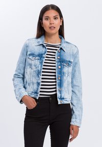 Jasnoniebieska kurtka dżinsowa z wyblakłym wzorem, z przednimi kieszeniami, zapięciem na guziki i klasycznym kołnierzykiem. Nosi się ją na czarno-białą bluzkę w paski.