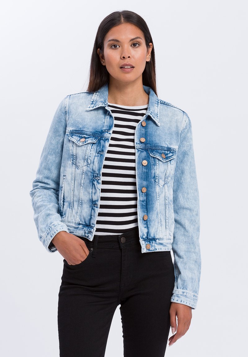 Jasnoniebieska kurtka dżinsowa z wyblakłym wzorem, z przednimi kieszeniami, zapięciem na guziki i klasycznym kołnierzykiem. Nosi się ją na czarno-białą bluzkę w paski.