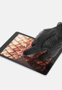 En svart läderhandske vilar på en surfplatta som visar ett strukturerat mönster. Surfplattan har en elegant design och en silverram.