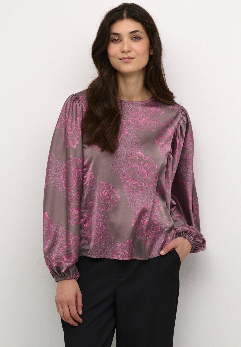 Satin blouse in grey with pink floral print, featuring long sleeves, gathered shoulders, and a loose fit. Paired with dark pants.
