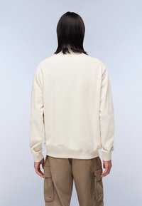 Cream-colored sweatshirt with a soft texture, ribbed cuffs, and a round neckline, paired with beige cargo pants featuring side pockets.