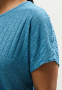 Lyhythihainen paita pehmeässä sinisessä kankaassa, jossa on hienovarainen raidoitus, rento istuvuus ja pyöreä pääntie.