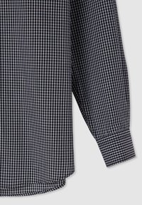 Camicia a maniche lunghe a scacchi bianco e nero con polsini abbottonati e orlo curvo, realizzata in un tessuto leggero.