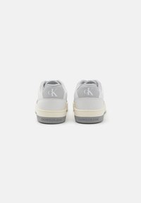 Sneakers bianchi con accenti grigi, dotati di una tomaia in pelle liscia, suola in gomma e dettagli del logo sul tallone e sul lato.