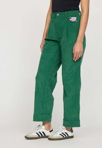 Pantalons en velours côtelé vert à taille haute, avec un pli avant et des manches retroussées. Comprend une poche plaquée avec un design coloré.