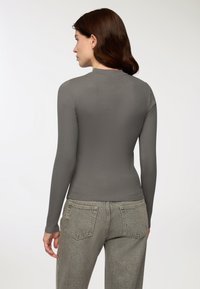 Szara bluza z długim rękawem o prążkowanej fakturze i wysokim dekolcie, połączona z jasnoszarymi dżinsami o subtelnym wzorze.