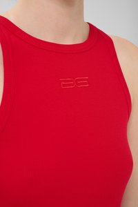 Débardeur rouge à rayures avec un col montant, présentant un logo en relief sur la poitrine. Le matériau semble lisse avec une coupe ajustée.