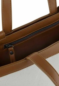 Canvas tas met bruine nepleren handgrepen en afwerking. Binnenin bevindt zich een zak met ritssluiting met een zwarte rits en een bruine voering.