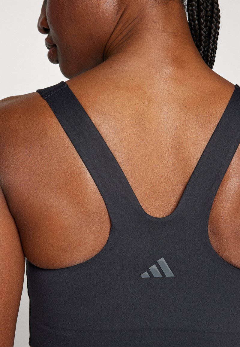 Soutien-gorge de sport noir avec un design dos nageur, fabriqué dans un tissu lisse et extensible. Inclut un détail de logo subtil à trois rayures.