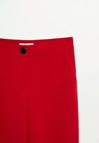 Pantalon rouge taille haute avec une fermeture à bouton noir et des poches latérales, présenté sur un fond blanc uni.