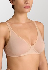 Bra wireless beige con spalline sottili e regolabili, scollatura profonda, coppe morbide senza cuciture e una consistenza liscia.