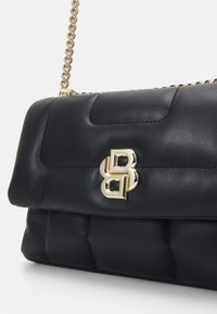Black quilted leather handbag with a gold chain strap and gold logo accent. Features a smooth texture and structured shape.