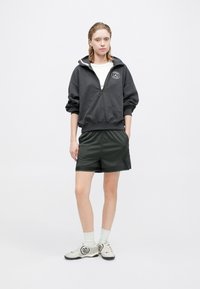 Grijze zip-up sweatshirt met een logo, gecombineerd met donkergroene shorts. Getextureerde stof, relaxte pasvorm en lichtgekleurde enkelsokken met schoenen.