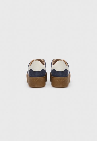 Μπλε ναυτικό και μπεζ σουέντ αθλητικά παπούτσια με υφή καφέ λαστιχένιας σόλας. Διαθέτουν καμπυλωτές λεπτομέρειες και λογότυπο στο πίσω μέρος.