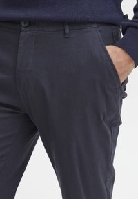 Dunkelmarineblaue Hose aus glattem Stoff, mit Seitentaschen und Knopfverschluss. Maßgeschneiderter Schnitt mit leichtem Glanz.