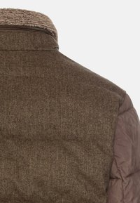 Brunt hørfrakke i sildebensmønster med uld på bagsiden, med en beige fleecekrave og et glat brunt pufferafsnit på skuldrene.