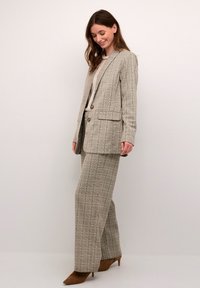 Traje de cuadros beige con un blazer ajustado y pantalones de pierna ancha, que presenta una textura suave y acentos en gris claro, combinado con tacones marrones.