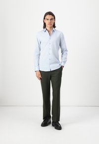 Light blue long-sleeve button-up shirt paired with dark green trousers and black shoes. Smooth fabric, tailored fit, and straight-cut design.